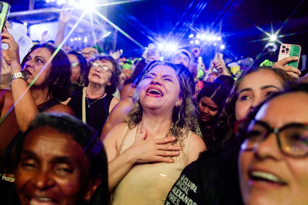 A foto mostra uma parte da multidão que aproveitou os shows do aniversário de Fortaleza no Aterrinho. Em destaque aparece uma mulher cantando.